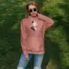Femme portant un hoodie rose avec un design artistique féminin, idéal pour un look moderne et élégant.
