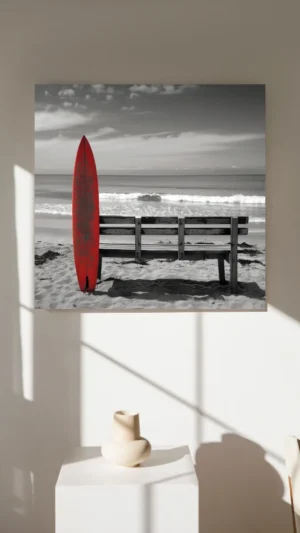 Planche de surf rouge appuyée contre un banc en bois sur une plage déserte.