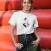 Femme portant un t-shirt blanc avec un dessin artistique représentant une femme élégante et des fleurs rouges, parfait pour un look chic et moderne.